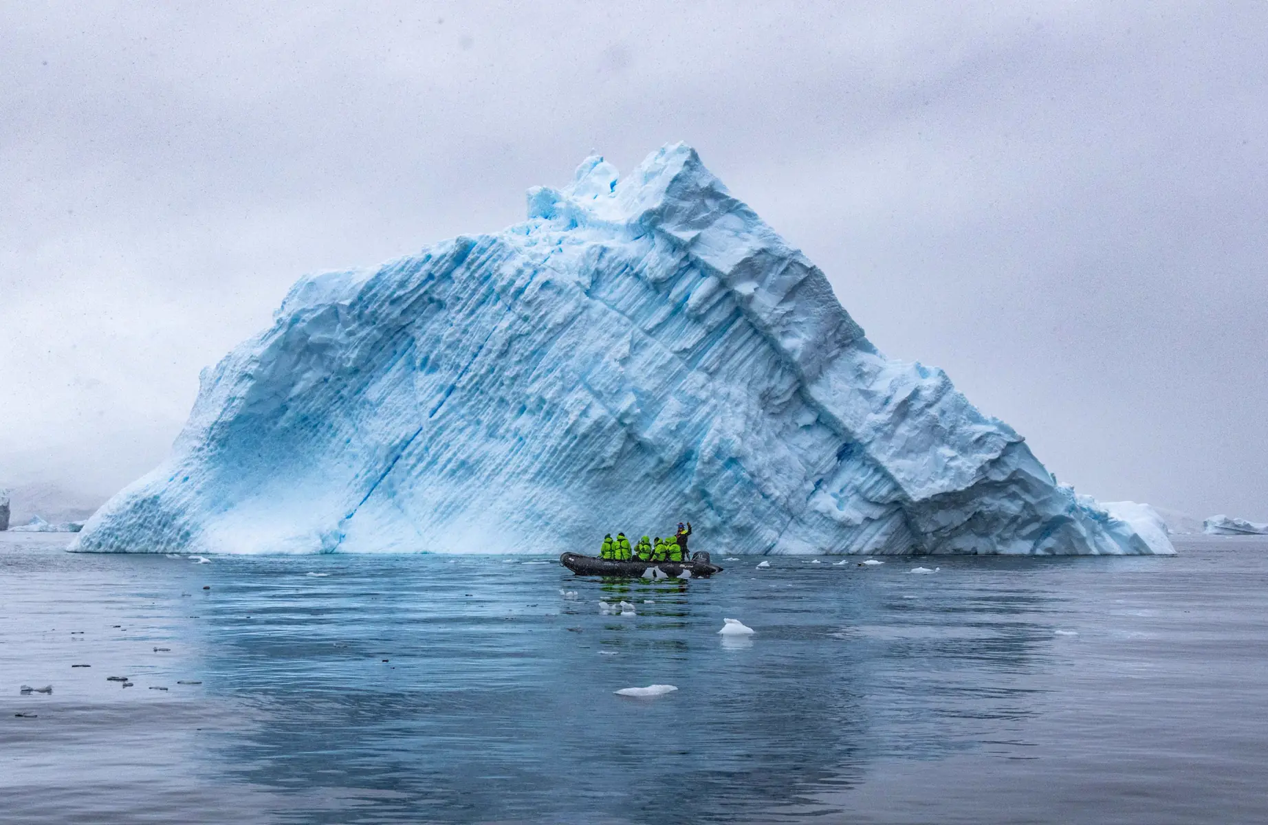 A small boat of travellers beside a towering blue iceberg