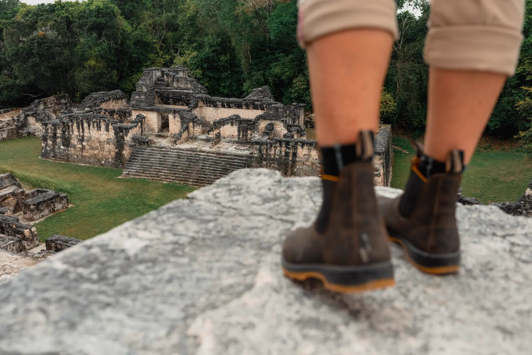 Hiking boots on a stone ledge overlooking Maya ruins