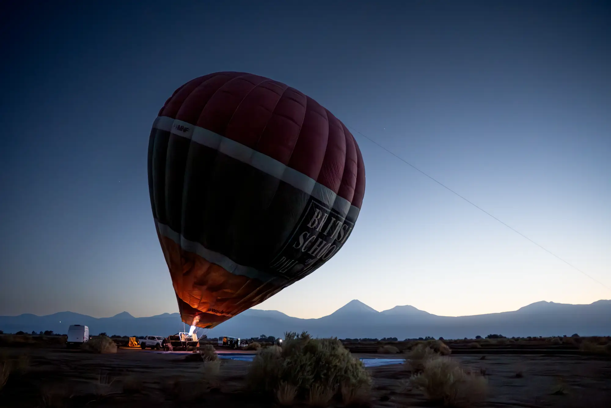 A hot-air balloon lifting off at dawn below the Andes