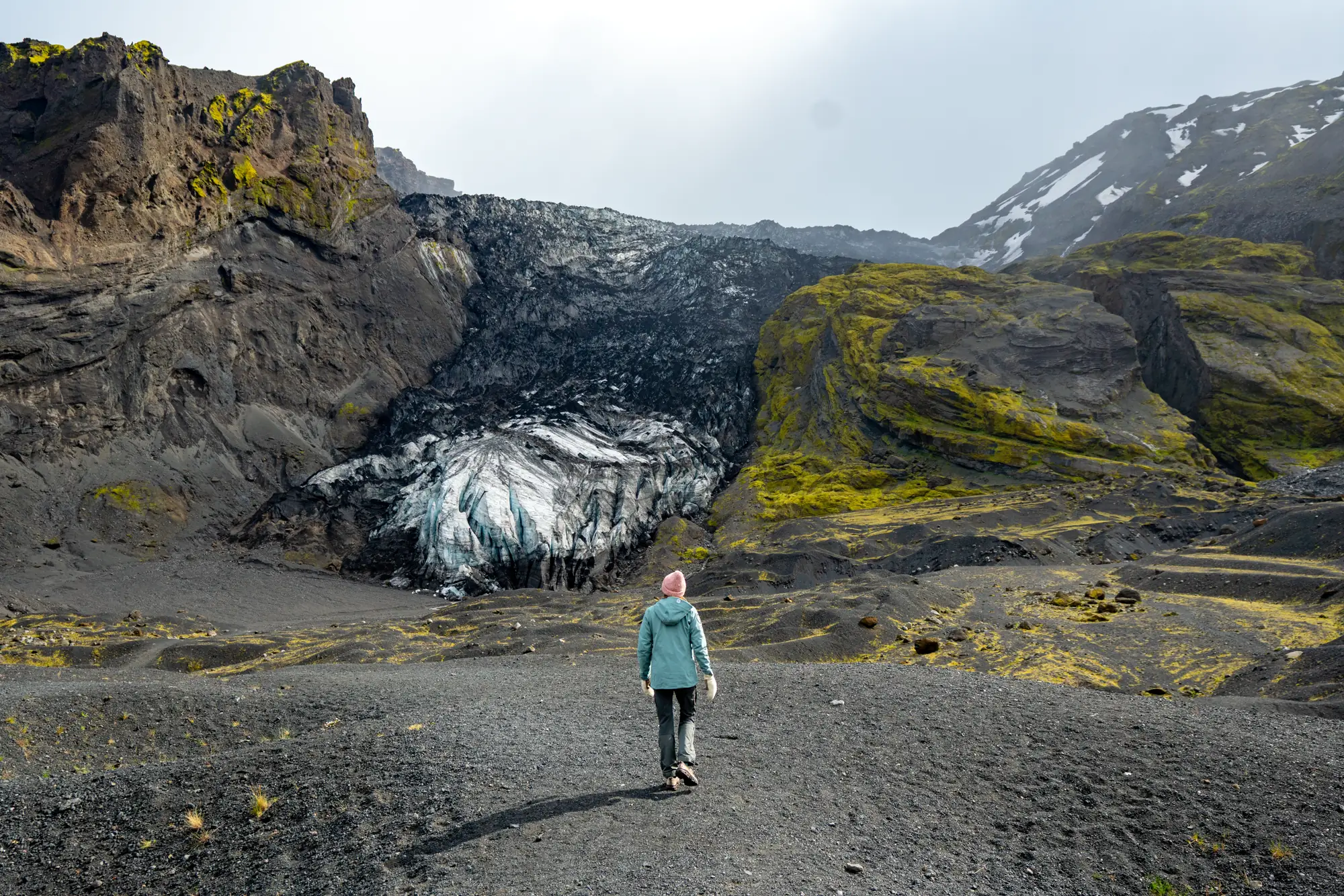 A traveller walking toward a glacier tongue between volcanic slopes