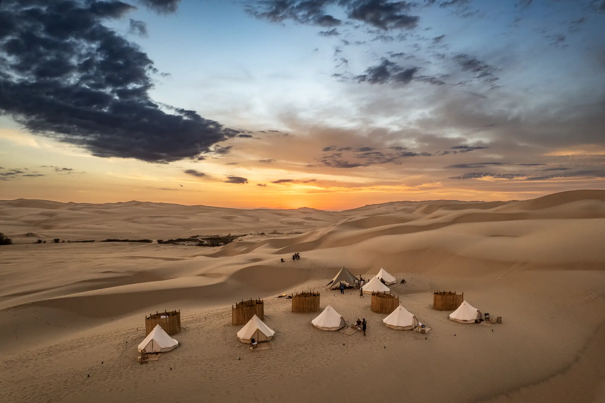 A private camp of bell tents among desert dunes at sunset