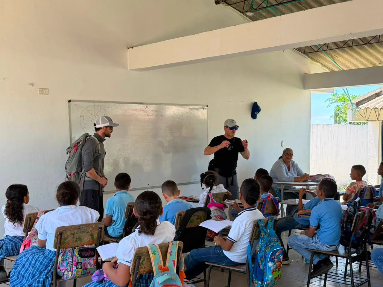 Students in a classroom listening to two visitors by the whiteboard