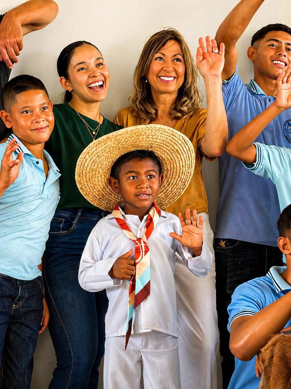Children and adults from the community laughing together; a boy in a sombrero vueltiao waves at the camera
