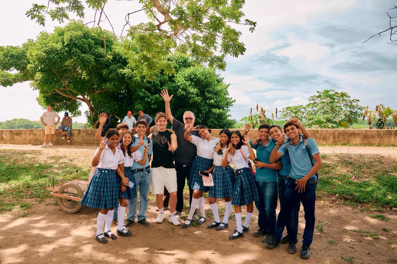 A group of students in school uniforms smiling and waving at the camera alongside Foundation partners