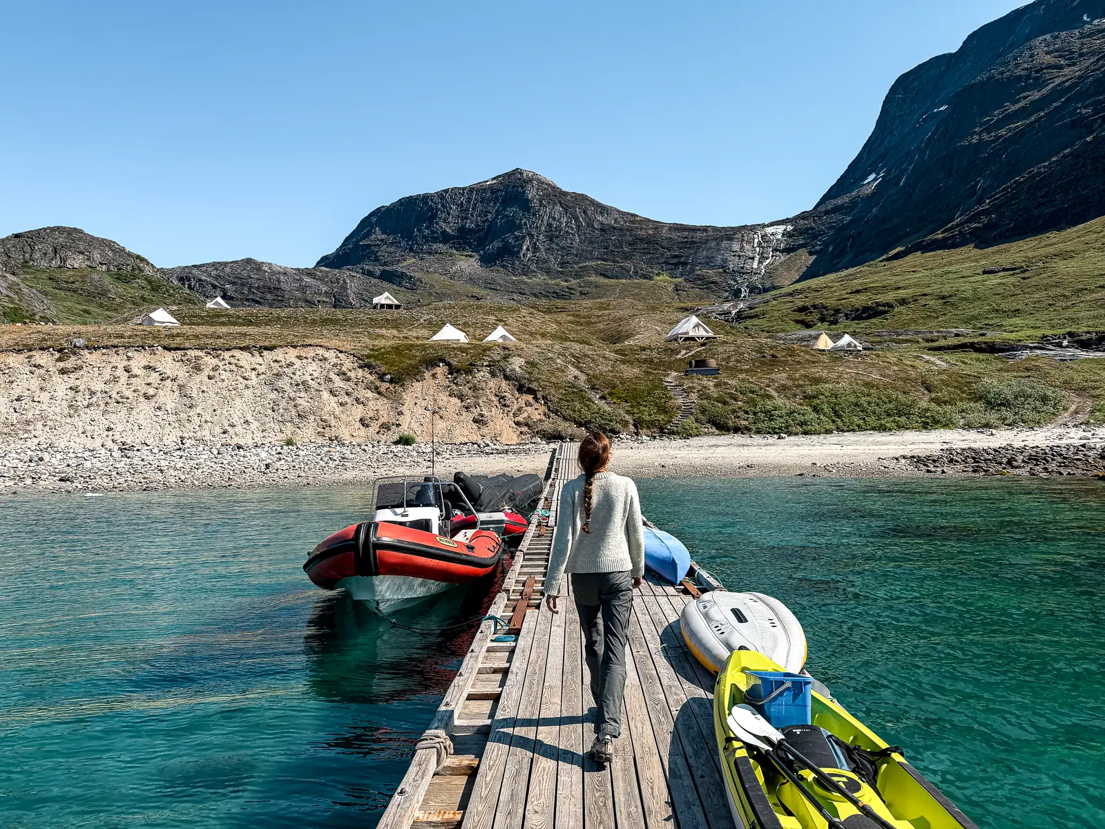 A wooden landing dock lined with zodiacs and kayaks, leading to a remote camp in Greenland